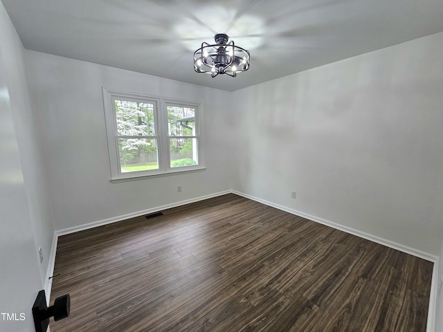 empty room featuring baseboards, dark wood-style flooring, a notable chandelier, and visible vents