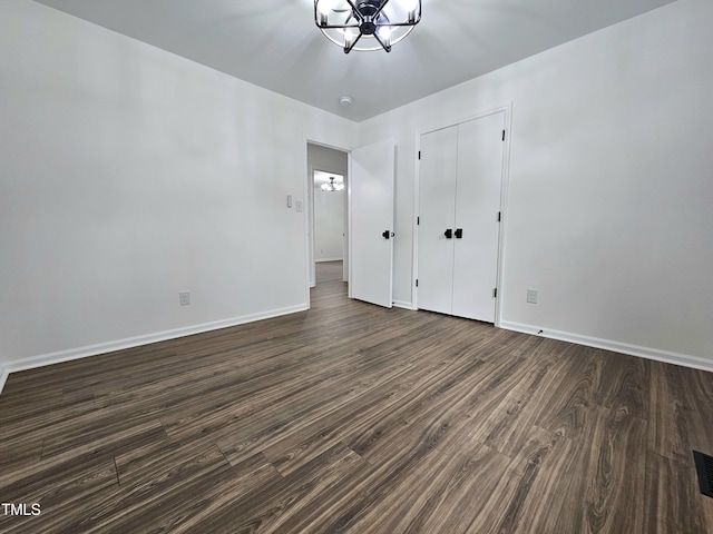 unfurnished bedroom with a closet, baseboards, a chandelier, dark wood-type flooring, and visible vents