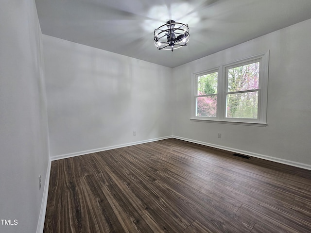 unfurnished room with visible vents, baseboards, an inviting chandelier, and dark wood-style floors
