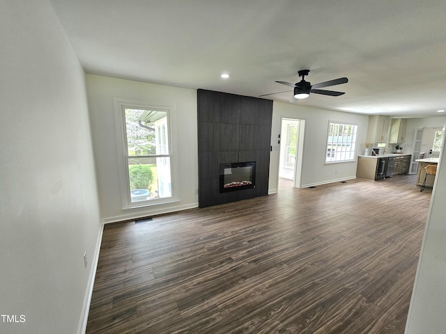 unfurnished living room featuring baseboards, ceiling fan, a fireplace, and dark wood finished floors