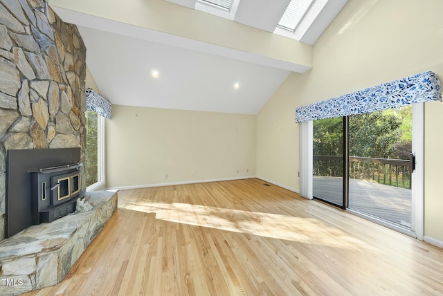 unfurnished living room with a skylight, a wood stove, wood finished floors, beam ceiling, and baseboards
