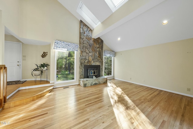 unfurnished living room with a skylight, high vaulted ceiling, wood finished floors, beamed ceiling, and a stone fireplace