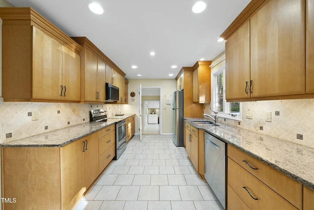 kitchen featuring appliances with stainless steel finishes, light stone counters, a sink, baseboards, and recessed lighting