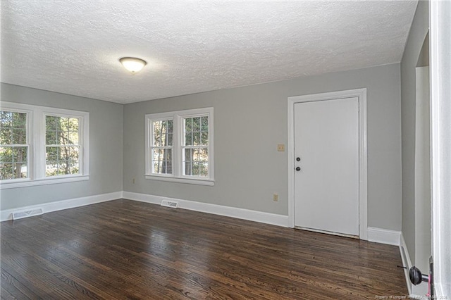 unfurnished room with baseboards, dark wood-type flooring, visible vents, and a textured ceiling