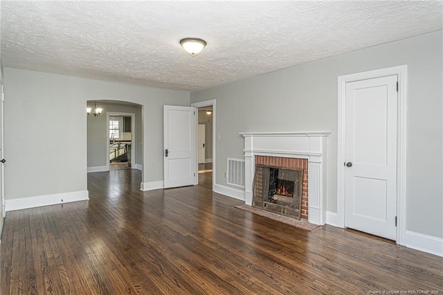 unfurnished living room featuring arched walkways, a textured ceiling, visible vents, a fireplace, and wood-type flooring