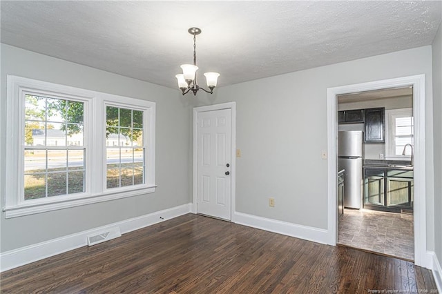 unfurnished dining area with dark wood-type flooring, a chandelier, visible vents, and baseboards