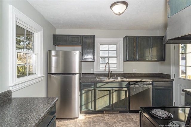 kitchen featuring a wealth of natural light, a sink, dark countertops, extractor fan, and appliances with stainless steel finishes