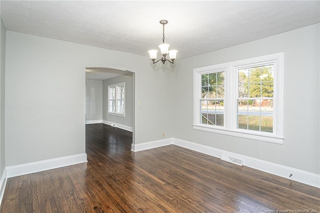 spare room with dark wood-style floors, arched walkways, plenty of natural light, visible vents, and a notable chandelier