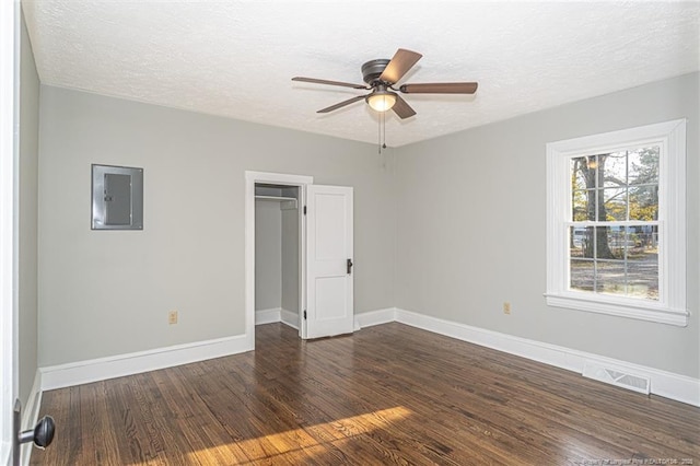 empty room featuring wood finished floors, a textured ceiling, electric panel, baseboards, and visible vents