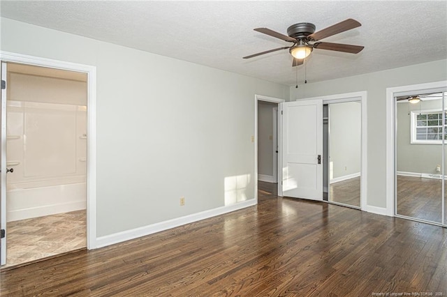 unfurnished bedroom with multiple closets, wood finished floors, connected bathroom, baseboards, and a textured ceiling