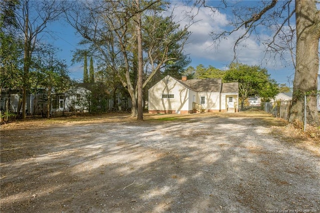 view of front of house with dirt driveway, a chimney, and fence