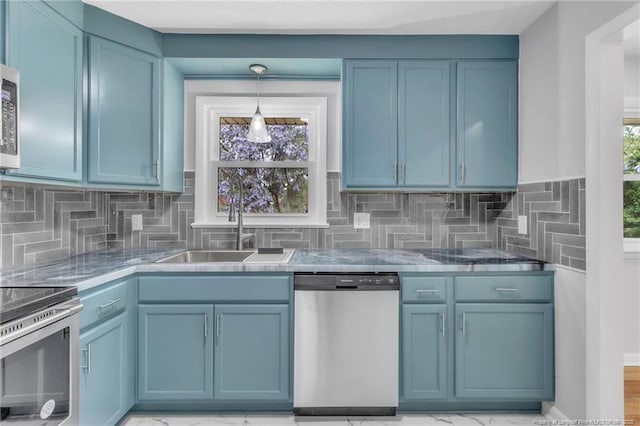 kitchen with a sink, backsplash, appliances with stainless steel finishes, decorative light fixtures, and blue cabinetry