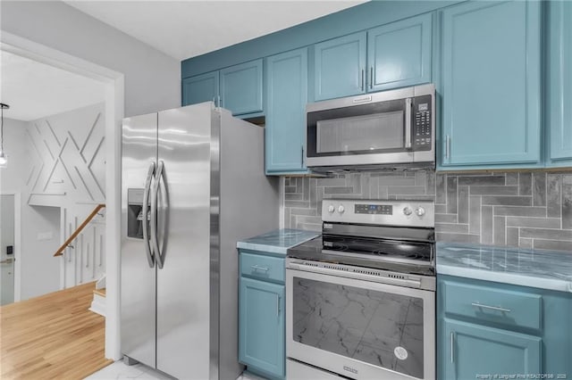 kitchen with tasteful backsplash, light countertops, appliances with stainless steel finishes, and blue cabinetry