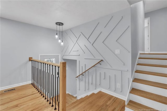 stairway featuring wood finished floors, baseboards, and visible vents
