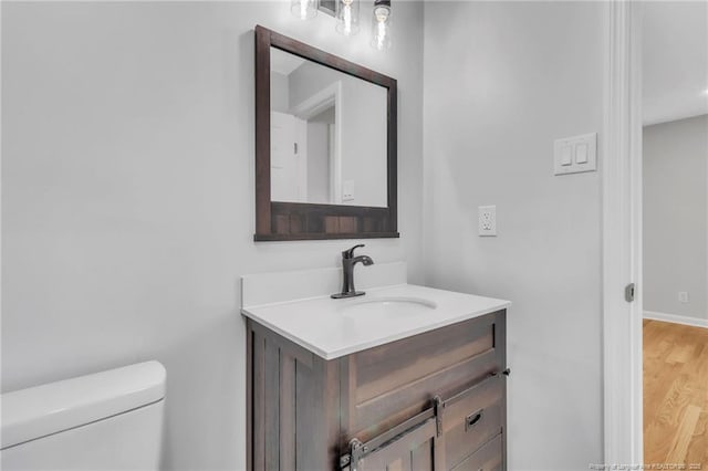 half bathroom featuring baseboards, wood finished floors, toilet, and vanity