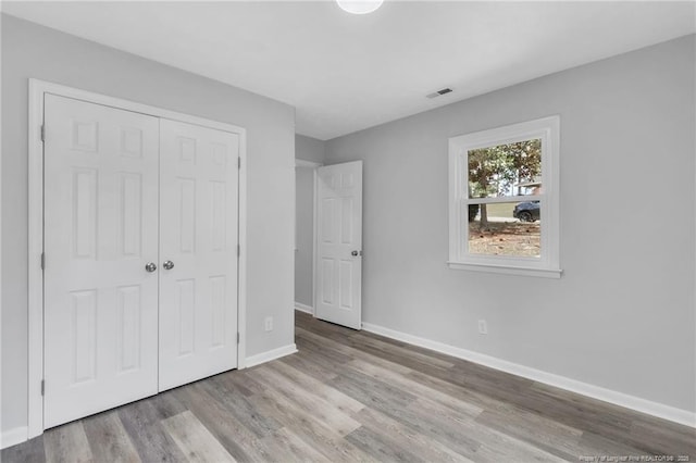 unfurnished bedroom with a closet, baseboards, visible vents, and wood finished floors