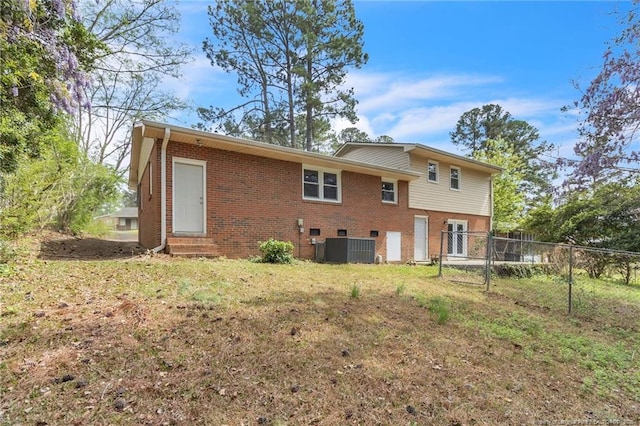 rear view of house with fence, central air condition unit, entry steps, brick siding, and a lawn