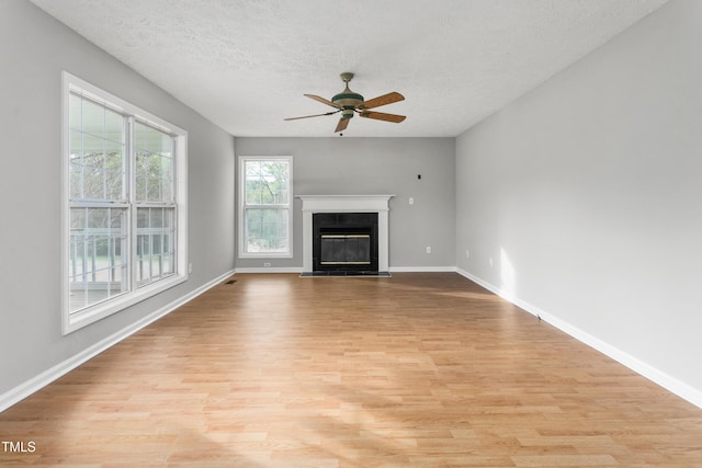 unfurnished living room featuring a textured ceiling, ceiling fan, baseboards, and light wood-type flooring