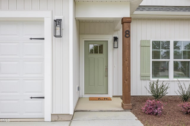 entrance to property featuring an attached garage, roof with shingles, and board and batten siding
