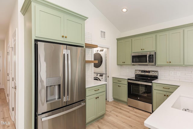 kitchen with decorative backsplash, stacked washer / dryer, appliances with stainless steel finishes, lofted ceiling, and green cabinetry