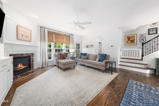living area with a ceiling fan, stairs, a fireplace, and dark wood finished floors