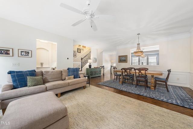 living room featuring stairs, wood finished floors, a ceiling fan, a chandelier, and wainscoting