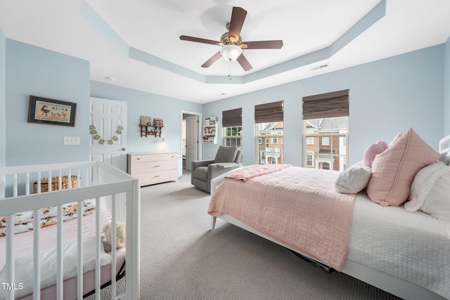 bedroom with a tray ceiling, light carpet, and a ceiling fan