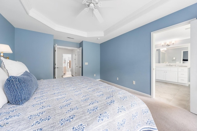 bedroom featuring a tray ceiling, crown molding, ensuite bathroom, light colored carpet, and a ceiling fan