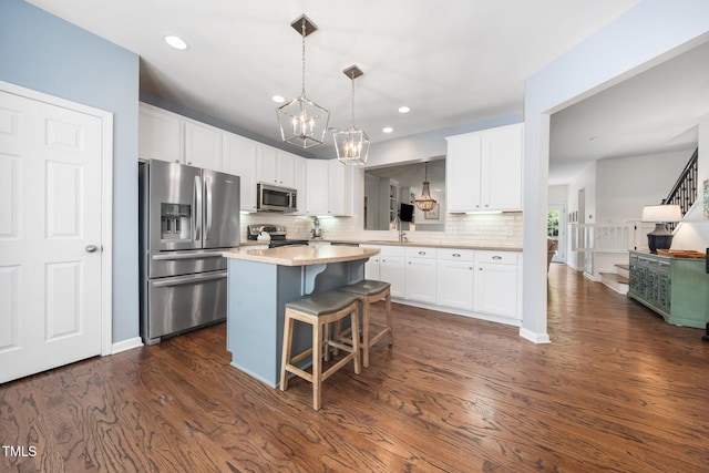 kitchen featuring appliances with stainless steel finishes, a chandelier, a kitchen island, tasteful backsplash, and white cabinets