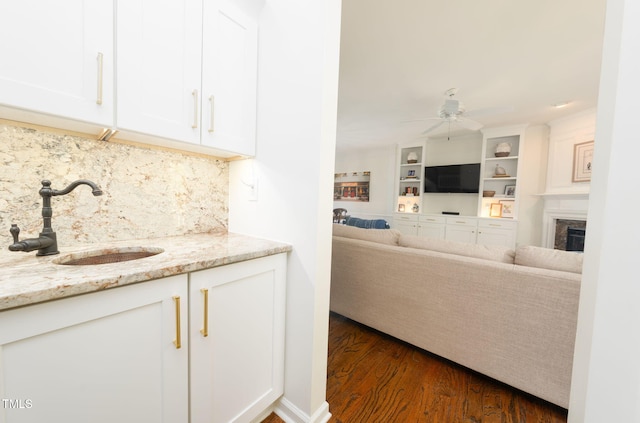 kitchen featuring a sink, a ceiling fan, dark wood-style flooring, light stone counters, and white cabinetry