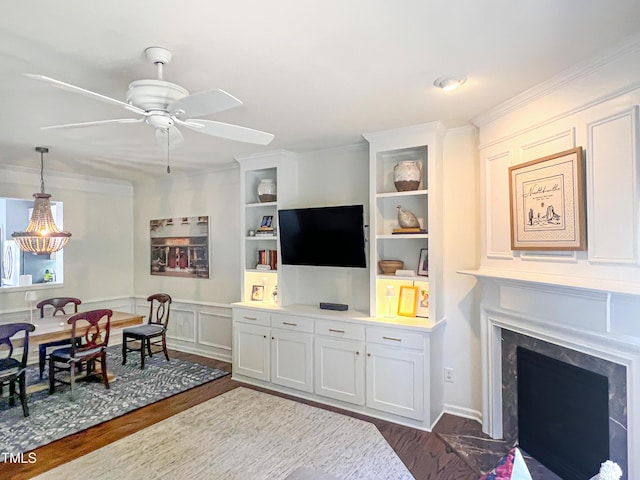 living room featuring dark wood-type flooring, a ceiling fan, a premium fireplace, built in features, and crown molding
