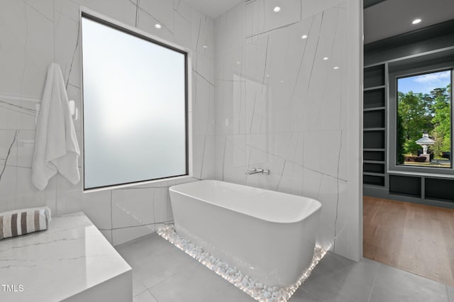 bathroom featuring a soaking tub, tile walls, and tile patterned floors