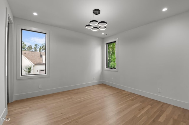 empty room with a chandelier, baseboards, light wood-type flooring, and recessed lighting