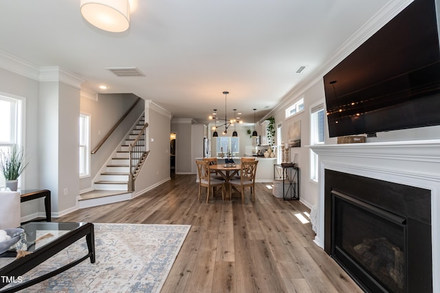 living room featuring stairs, ornamental molding, a fireplace, light wood-style flooring, and a chandelier