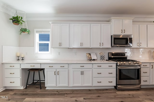 kitchen featuring stainless steel appliances, decorative backsplash, white cabinetry, ornamental molding, and light countertops