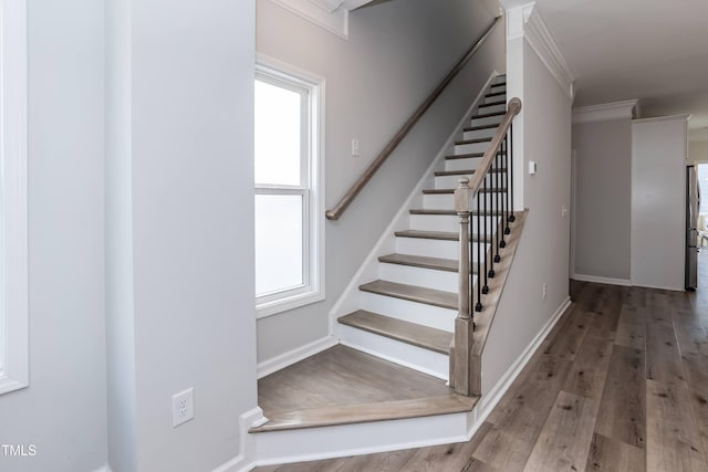 stairway with wood finished floors, baseboards, and crown molding