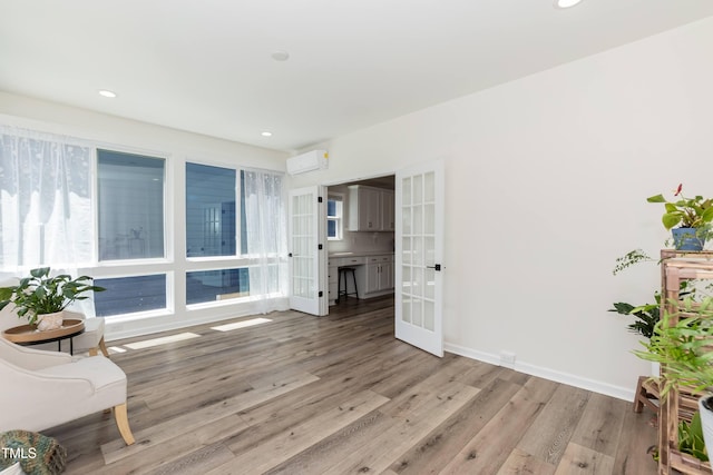 living area with french doors, a wall mounted air conditioner, wood finished floors, recessed lighting, and baseboards