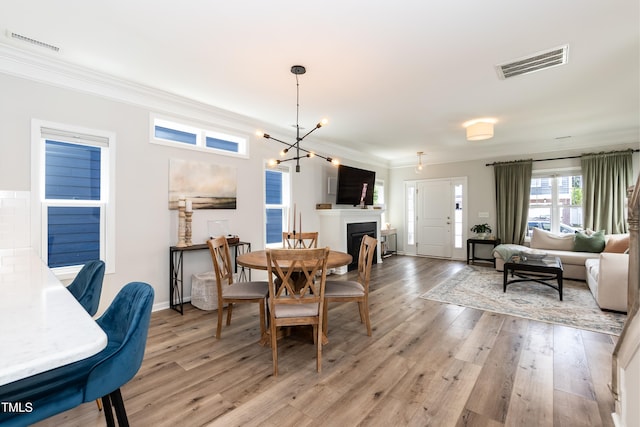 dining room with light wood-style floors, crown molding, a chandelier, a fireplace, and baseboards
