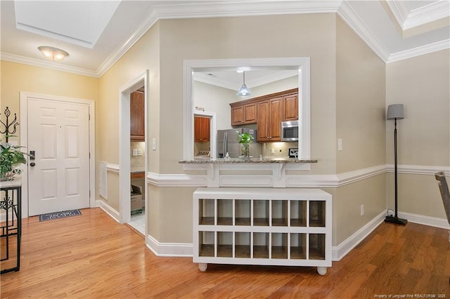 kitchen featuring a kitchen bar, light wood-type flooring, stainless steel appliances, ornamental molding, and brown cabinets