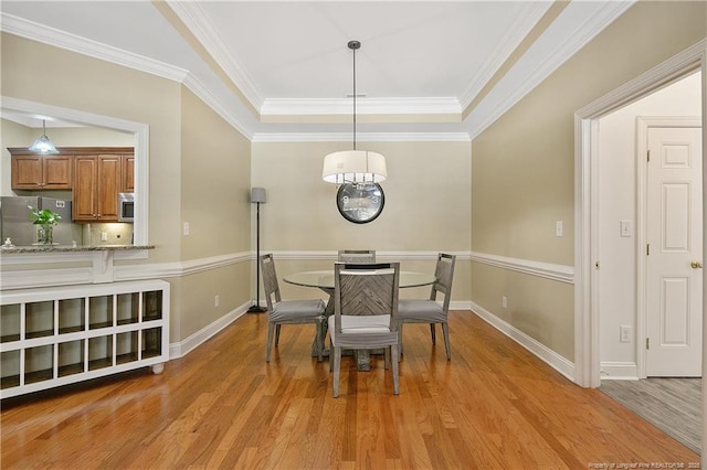 dining area with baseboards, light wood-type flooring, ornamental molding, and a raised ceiling