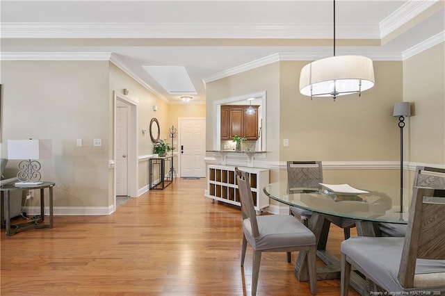 dining area featuring baseboards, crown molding, light wood-style floors, and a skylight