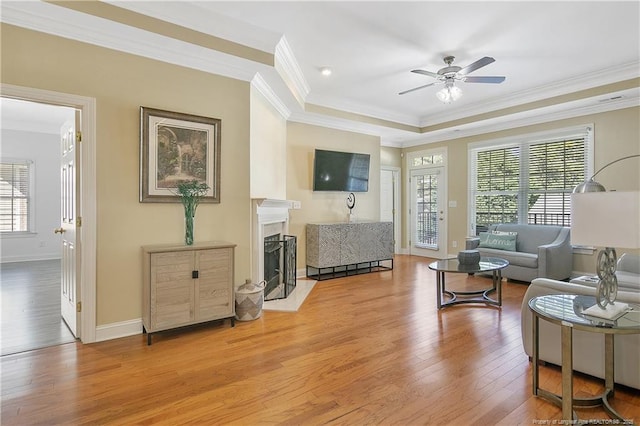 living area with a fireplace with flush hearth, ornamental molding, wood finished floors, and a ceiling fan