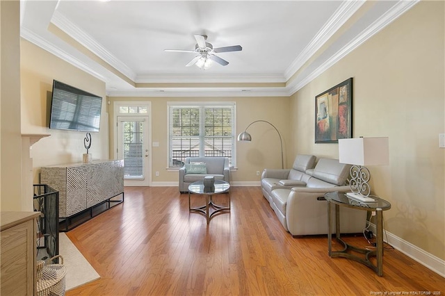 living room with ornamental molding, baseboards, a raised ceiling, ceiling fan, and wood finished floors