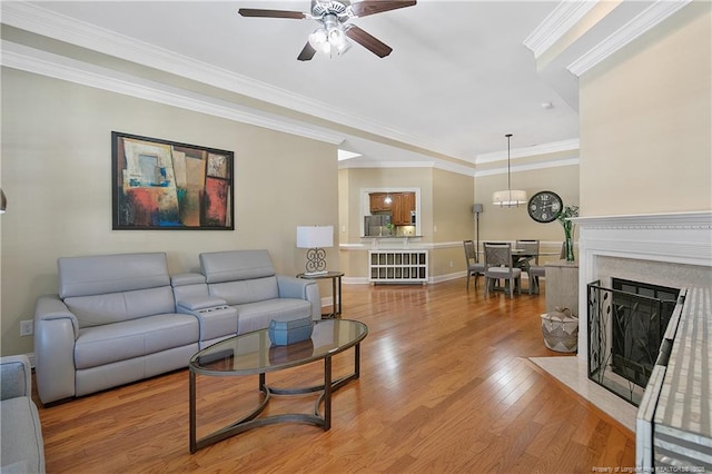 living area featuring a high end fireplace, light wood finished floors, baseboards, ornamental molding, and ceiling fan with notable chandelier