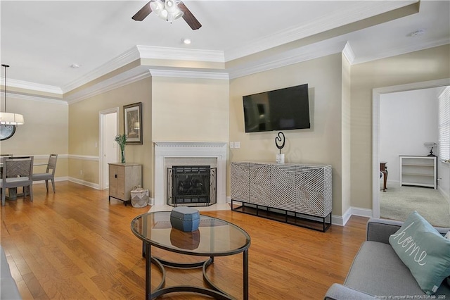 living area with baseboards, ornamental molding, wood finished floors, and ceiling fan with notable chandelier