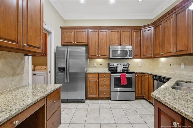 kitchen featuring ornamental molding, stainless steel appliances, washing machine and clothes dryer, light tile patterned flooring, and light stone countertops