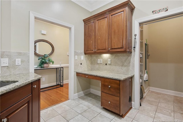 kitchen featuring built in desk, light tile patterned flooring, crown molding, and light stone countertops