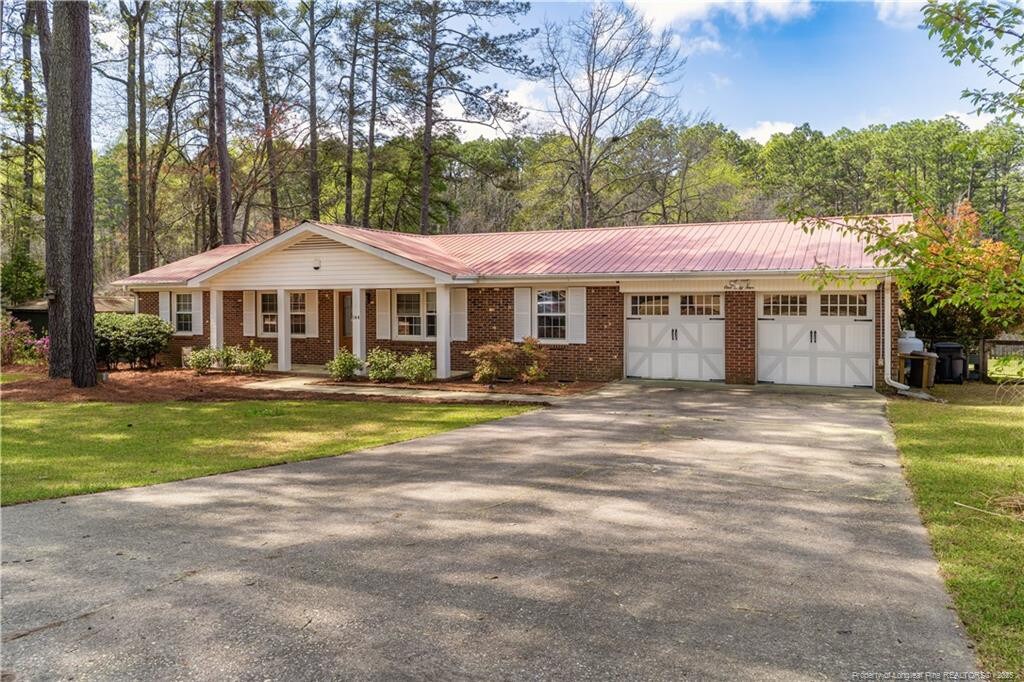 ranch-style home featuring driveway, a front yard, an attached garage, brick siding, and metal roof