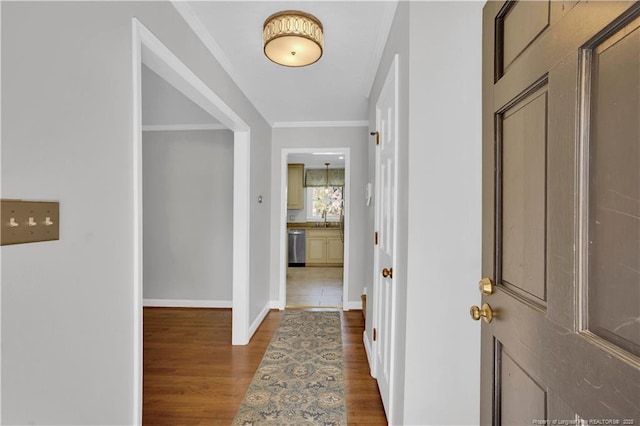corridor featuring dark wood-type flooring, baseboards, ornamental molding, and a sink