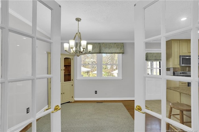 interior space with an inviting chandelier, wood finished floors, baseboards, and a textured ceiling